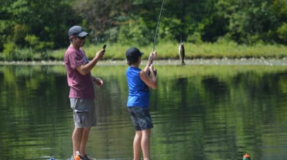 Staff and camper fishing on a lake dock.