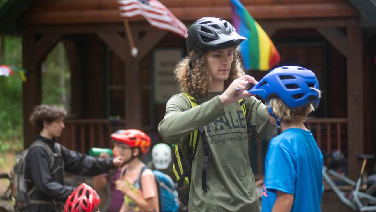 A man putting a helmet on a child in front of a cabin.