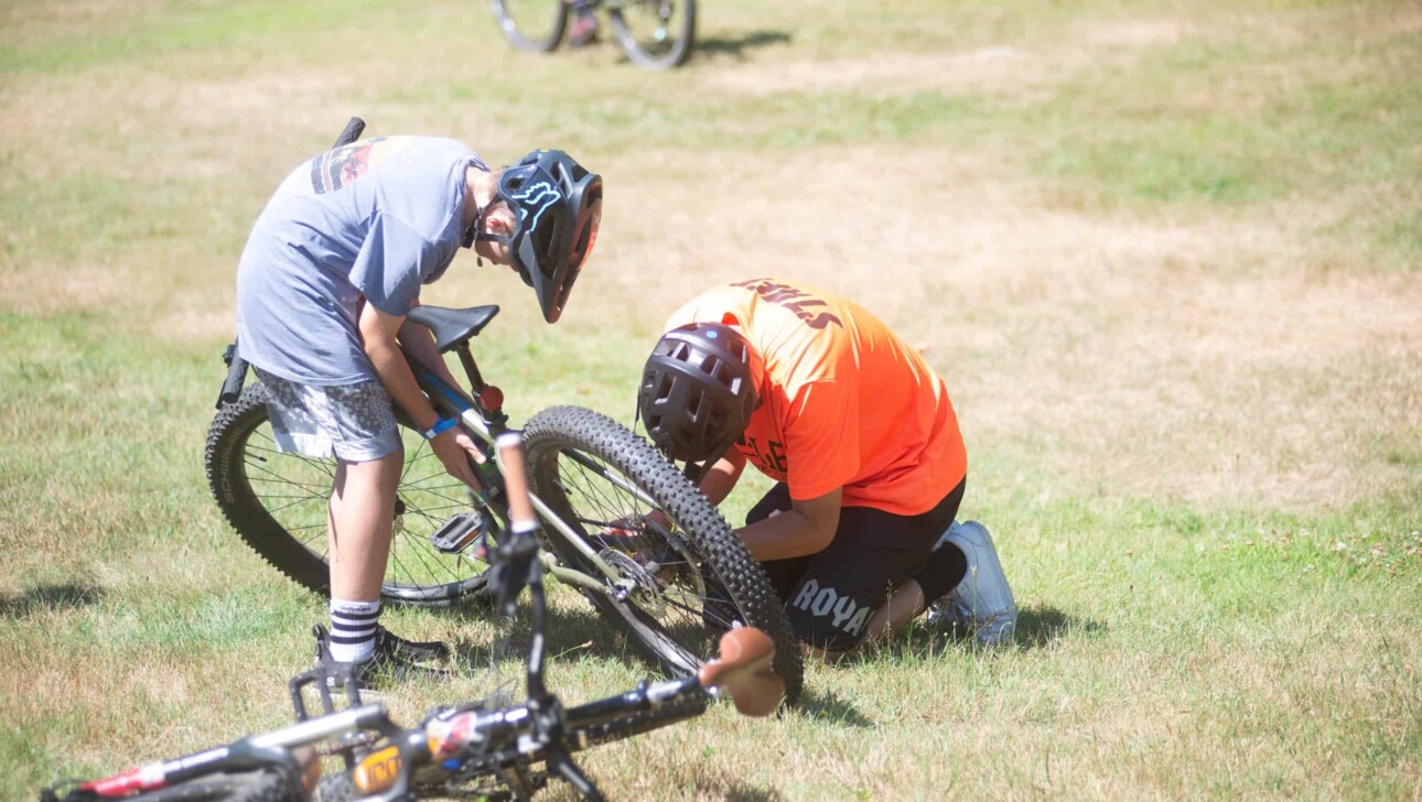 A group of people fixing a bike in the grass.
