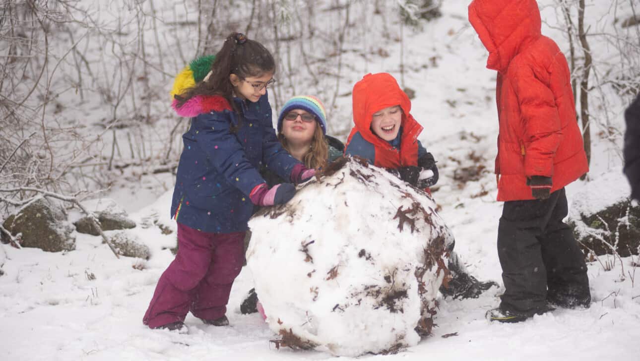 A group of children making a snowman in the woods.